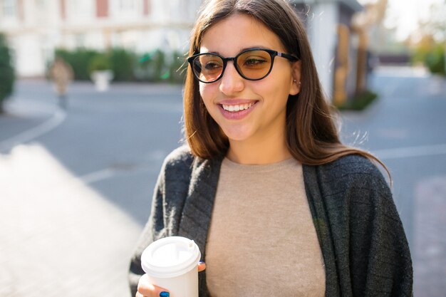 Meravigliosa donna elegante con occhiali da sole e caffè per andare a passeggiare per strada