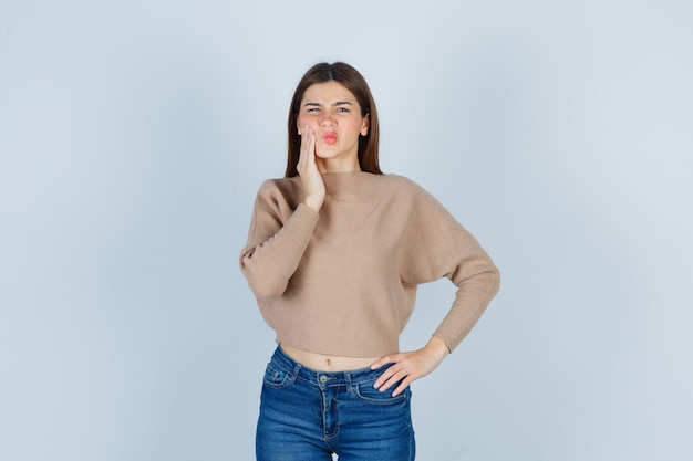 Meravigliosa signora che soffre di mal di denti in maglione, jeans e sembra dolorosa. vista frontale.