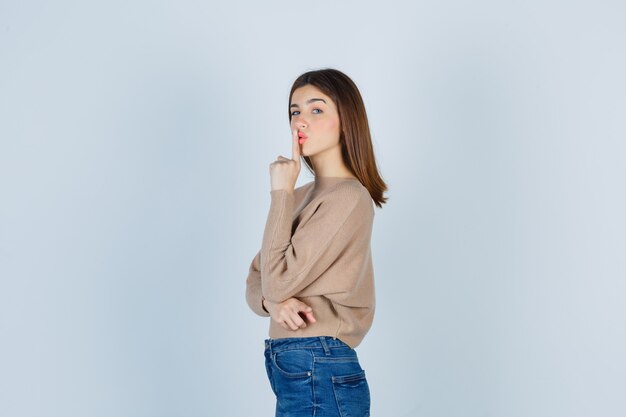 Meravigliosa signora in maglione, jeans che mostrano gesto di silenzio e sembrano cool.