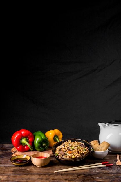 Mescolare tagliatelle fritte con verdure e pollo con peperoni; salse e involtini primavera sulla scrivania su sfondo nero