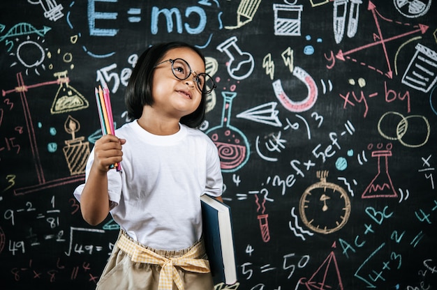 Messa a fuoco selettiva, bambina che indossa occhiali che tiene in mano una matita colorata e tiene in mano un grande libro di testo