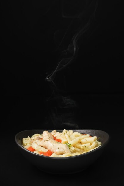 Messa a fuoco selettiva sulla zuppa di noodle al pollo piccante fatta in casa con verdure e spezie in una ciotola, primo piano, sfondo scuro.