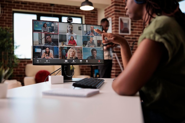 Messa a fuoco selettiva sullo schermo del computer con il team di avvio di dipendenti di avvio che lavorano a distanza in idee di brainstorming di videochiamate di gruppo. Donna afroamericana che gesturing nella riunione di Internet con i colleghi.