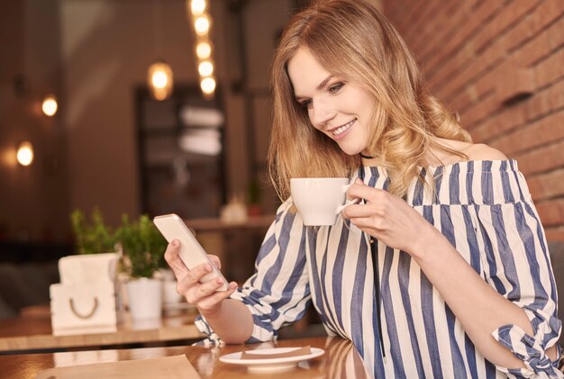 Messaggi di testo di una giovane donna mentre beve un caffè