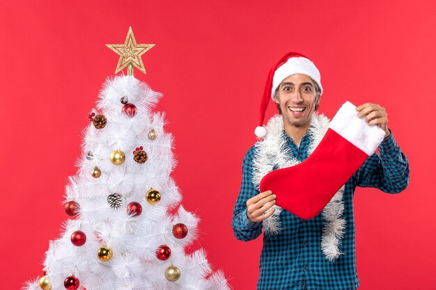 Metà corpo colpo di giovane uomo con cappello di Babbo Natale in una camicia blu spogliata e tenendo calzino di Natale