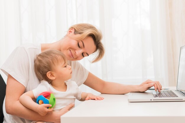 Metà del bambino della tenuta della madre del colpo che resta allo scrittorio e a sorridere