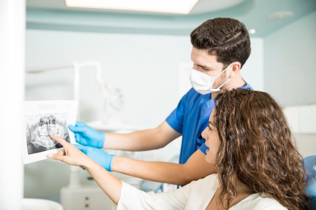 Metà del dentista adulto che mostra i raggi X dei denti al paziente femminile alla clinica odontoiatrica