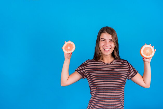 Metà della tenuta della giovane donna delle arance su fondo blu