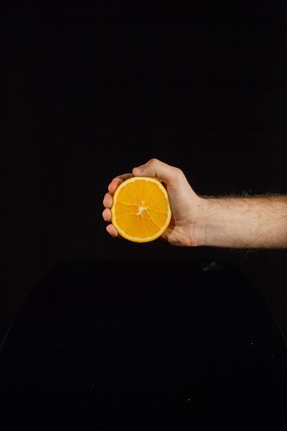 Metà di arancia succosa in mano dell&#39;uomo su sfondo nero
