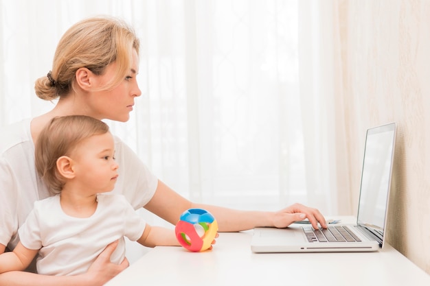 Metà di bambino della tenuta della madre del colpo che lavora allo scrittorio