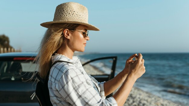 Metà di donna del colpo che prende le foto del mare in macchina