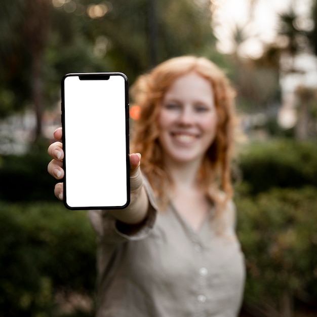 Metà di donna del colpo che tiene telefono in bianco