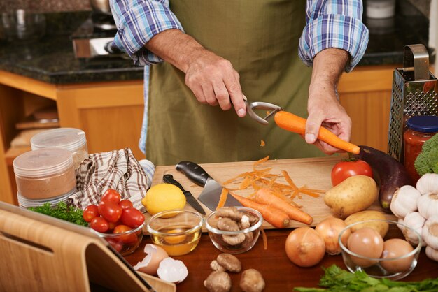 Metà di sezione del cuoco irriconoscibile che prepara gli ingredienti per il piatto della cena che raschia le carote