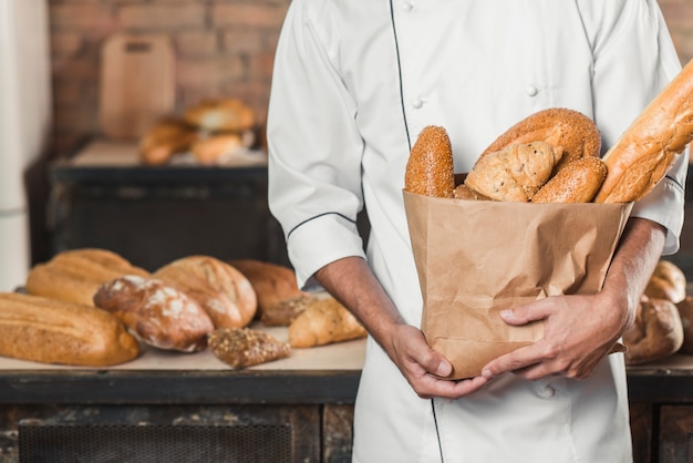 Metà di sezione del panettiere maschio che tiene sacchetto di carta con i pani