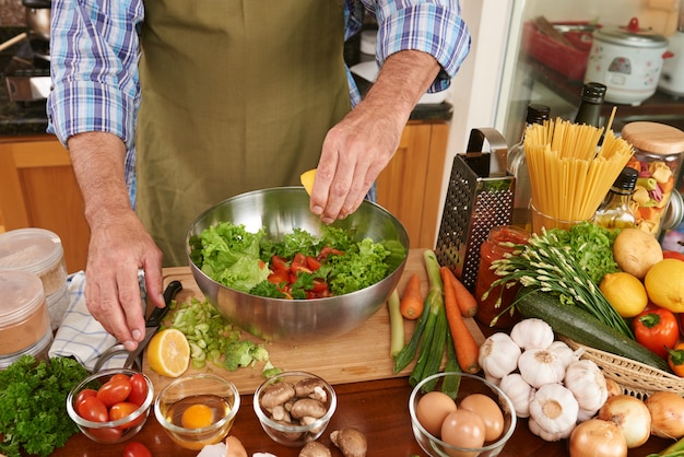 Metà di sezione dell'uomo irriconoscibile in grembiule che aggiunge il succo di limone all'insalata fresca