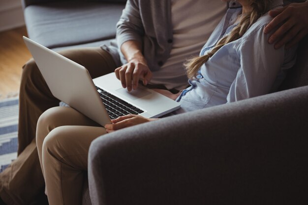 Metà di sezione della coppia utilizzando il computer portatile in soggiorno