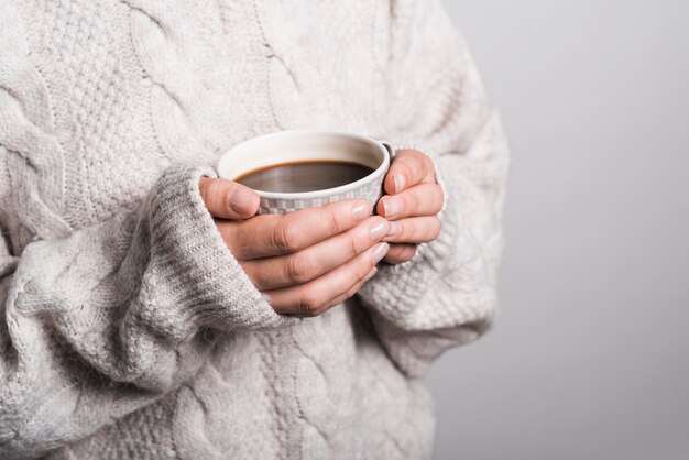 Metà di sezione della donna in vestiti di lana che tengono tazza di caffè