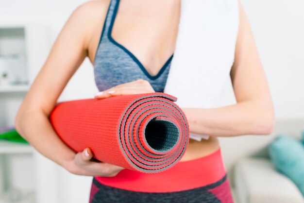 Metà di sezione della giovane donna di forma fisica che tiene la stuoia di esercizio rossa