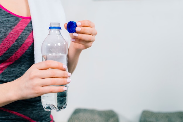 Metà di sezione della mano della giovane donna di forma fisica che tiene bottiglia di acqua di plastica trasparente