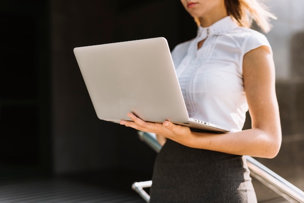 Metà di sezione di giovane donna di affari che tiene computer portatile all&#39;aperto