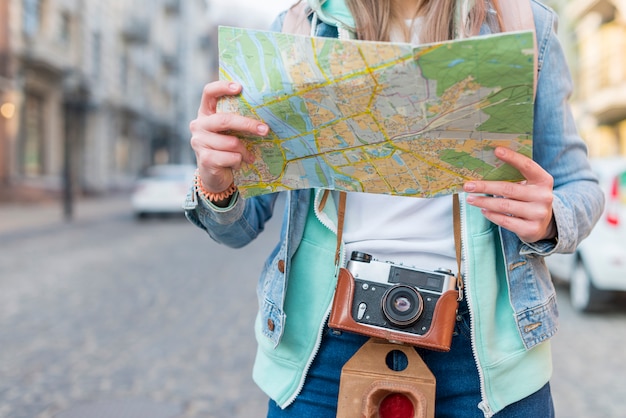 Metà di sezione di un viaggiatore femminile con la mappa della tenuta della macchina fotografica a disposizione