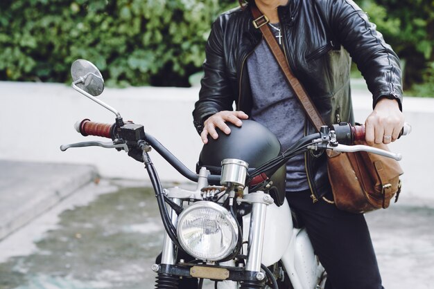 Metà di sezione di uomo irriconoscibile in giacca di pelle con casco seduto su una moto