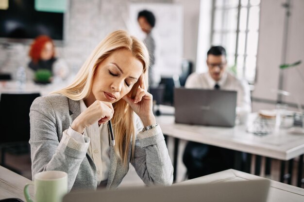 Metà donna d'affari adulta sentirsi esausta mentre lavora in ufficio Ci sono persone in background