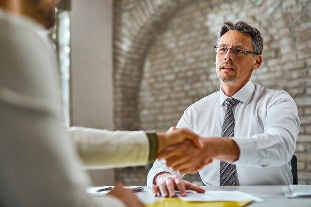 Metà manager adulto che stringe la mano a un candidato durante il colloquio di lavoro in ufficio