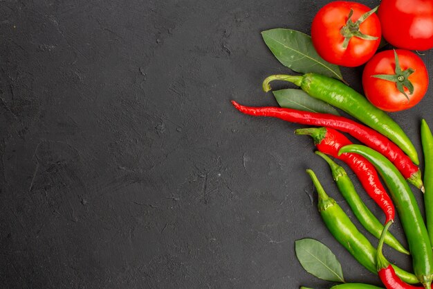 Metà superiore vista peperoni rossi e verdi caldi e foglie di alloro pomodori sul lato destro della terra nera