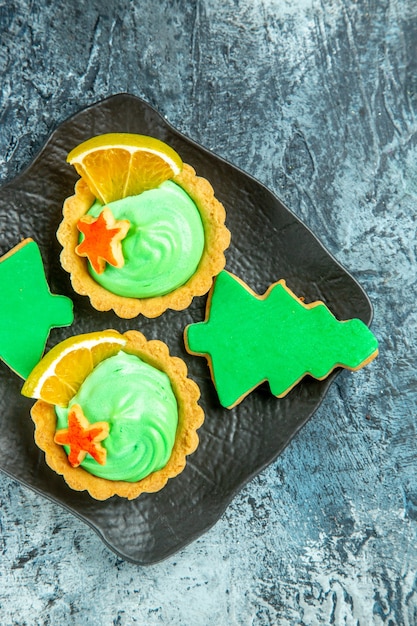 Metà superiore vista piccole crostate con biscotti dell'albero di Natale crema pasticcera verde sulla banda nera su superficie grigia