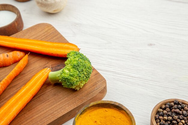 Metà vista inferiore carote e broccoli tritati sul tagliere funghi spezie diverse in ciotole sul posto libero del tavolo