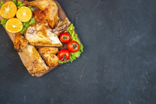 Mezza vista dall'alto pollo arrosto pomodori fette di limone su tavola di legno su nero