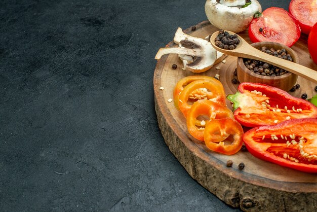 Mezza vista inferiore verdure fresche funghi pepe nero in una ciotola cucchiaio di legno pomodori rossi peperoni su tavola di legno su tavolo scuro con spazio libero