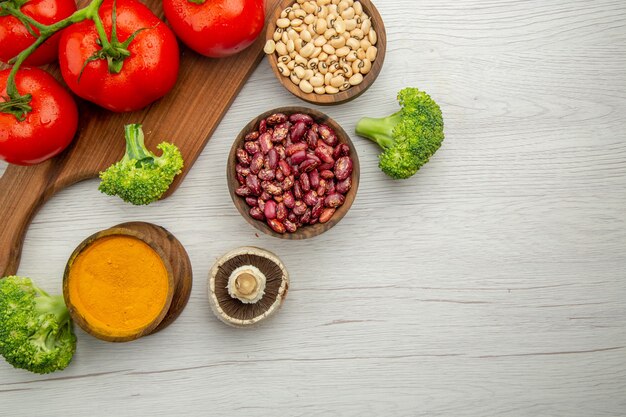 Mezza vista superiore ramo di pomodoro sul tagliere funghi broccoli fagioli ciotole curcuma sul tavolo spazio libero