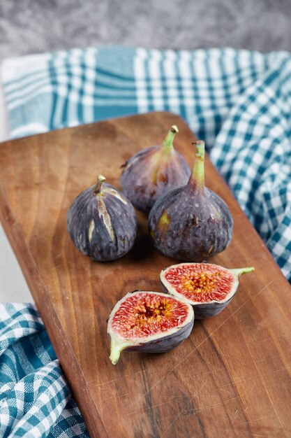 Mezze fette e fichi interi su tavola di legno con una tovaglia blu.