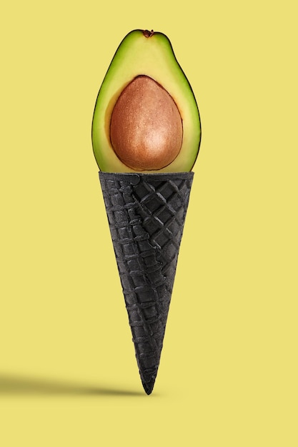 Mezzo avocado maturo con nocciolo in cono di cialda nero dolce su sfondo beige. Concetto di alimentazione sana, cibo, raccolto stagionale di frutta e verdura. Primo piano, copia spazio