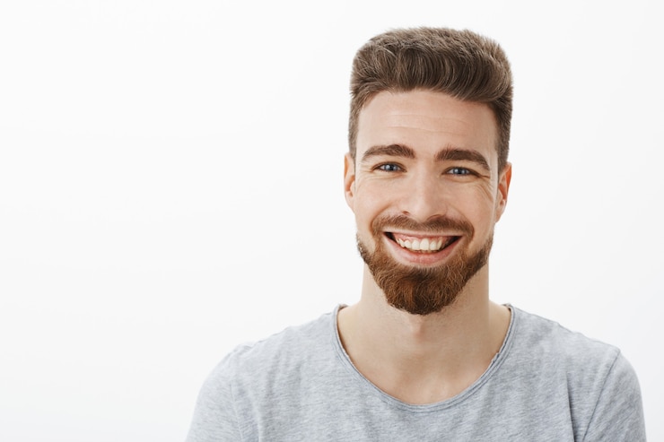 Foto gratuito mezzo busto di affascinante bell'uomo spensierato e ottimista con barba, baffi e occhi azzurri carini che ride gioiosamente strizzando gli occhi dalla gioia e dal divertimento divertendosi contro il muro grigio