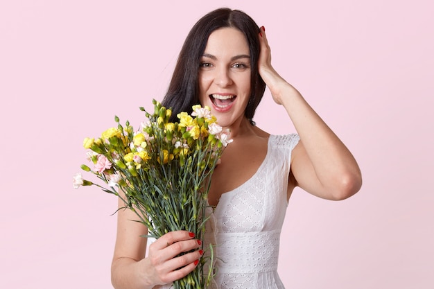 Mezzo busto di donna bella mora con mazzo di fiori, ridendo guardando direttamente la telecamera, tiene la mano sulla testa