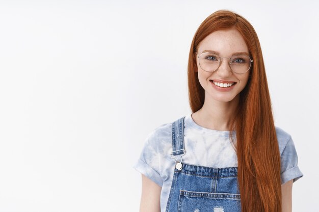 Mezzo busto fiducioso di bell'aspetto casual rossa ragazza occhi azzurri lungo rosso acconciatura naturale, esprimere felicità determinata ricevere il primo premio, fortunato umore ottimista, stare in piedi muro bianco sicuro di sé