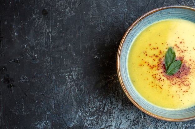 Mezzo colpo di deliziosa zuppa servita con pepe e menta in una pentola blu sul lato sinistro su sfondo scuro