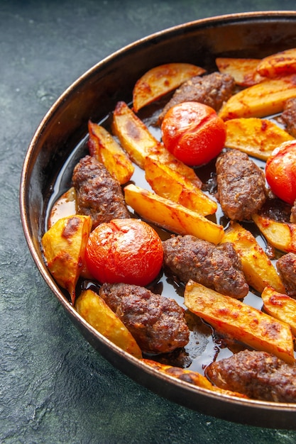 Mezzo colpo di deliziose cotolette di carne al forno con patate e pomodori su sfondo di colore verde e nero misto