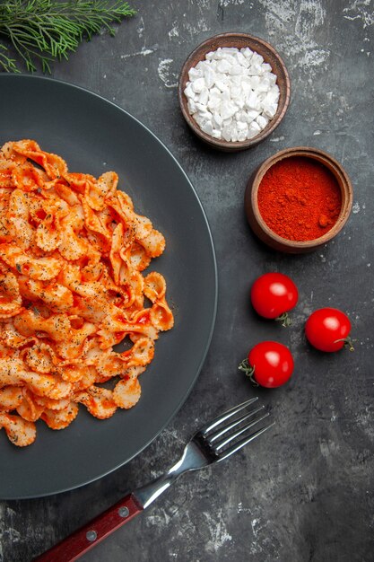 Mezzo colpo di pasta facile per cena su un piatto nero e forchetta su diverse spezie e pomodori su un tavolo scuro dark