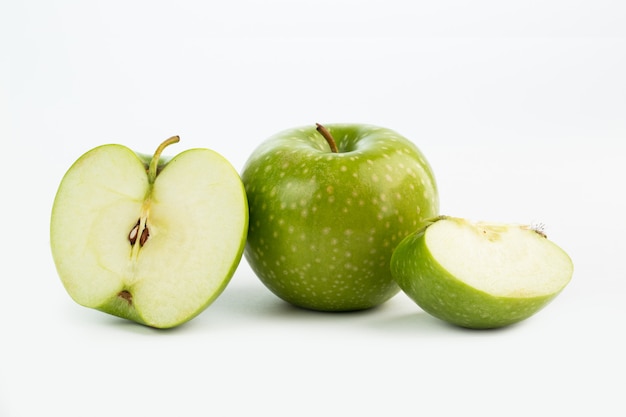 Mezzo taglio e pezzi verdi succosi freschi freschi della mela della frutta sul pavimento bianco