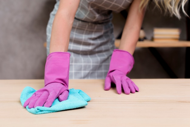 Midsection di un bidello femminile che pulisce la tavola di legno con il panno