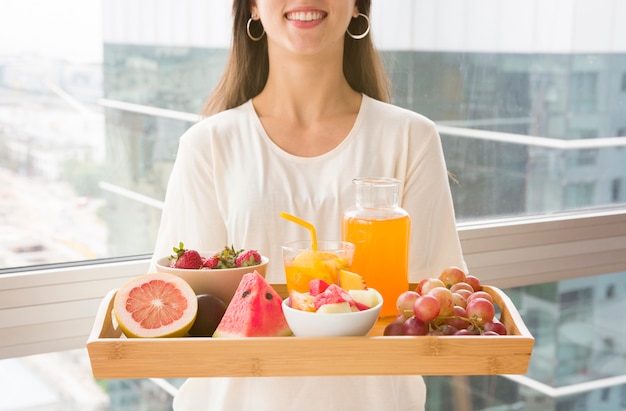 Midsection di una donna che tiene vassoio di legno con molti frutti e succo