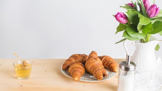 Miele; croissant al forno e vaso sullo scrittorio di legno contro fondo bianco