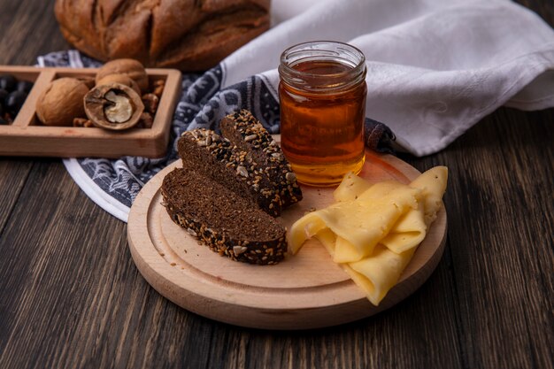 Miele di vista frontale in un vaso con pane nero e formaggio su un supporto con le noci su un fondo di legno