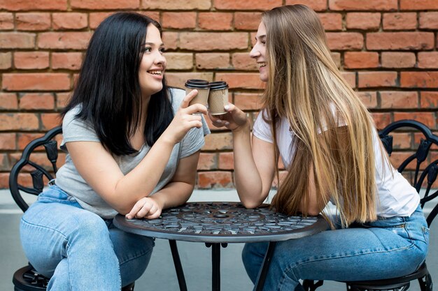 Migliori amici che esultano con bicchieri di caffè fuori