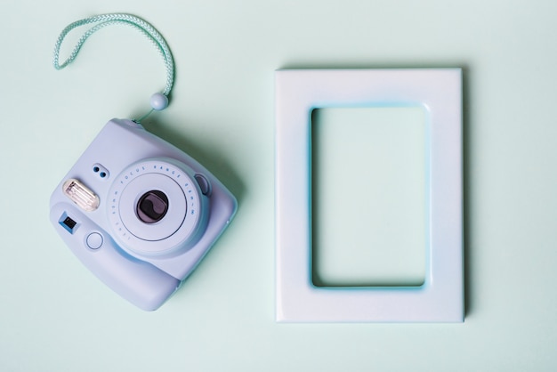 Mini macchina fotografica istantanea e cornice vuota bordo su sfondo blu