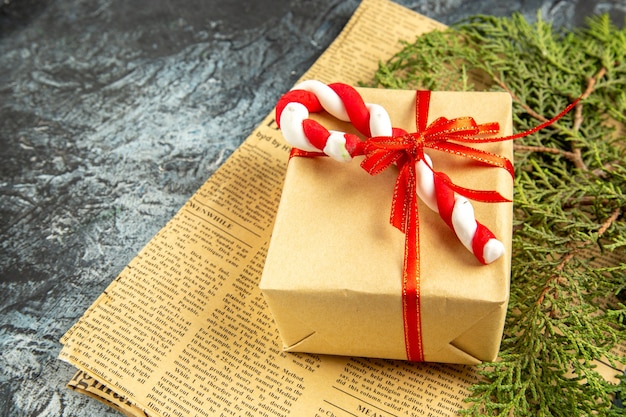 Mini regalo vista dal basso legato con nastro rosso caramelle natalizie su giornale su sfondo grigio